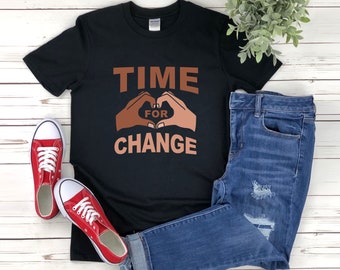 May include: Black t-shirt with the text "TIME FOR CHANGE" in brown letters. The text is surrounded by two brown hands forming a heart shape.