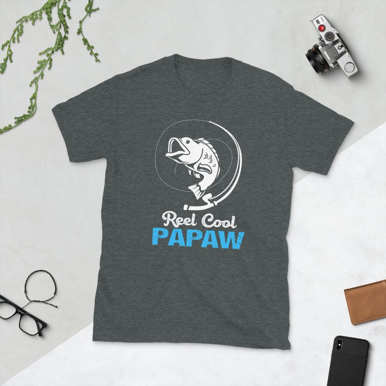 May include: A dark gray t-shirt with a white graphic of a fish being reeled in. The text "Reel Cool Papaw" is printed in blue below the graphic.