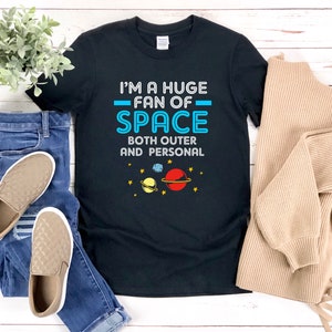 May include: Black t-shirt with the text "I'm a huge fan of space, both outer and personal" in white and blue. The shirt features a graphic of planets and stars.