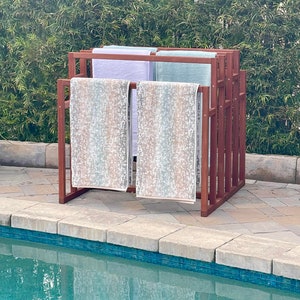 May include: A wooden towel rack with four towels hanging on it. The towels are white, light blue, and a light blue and brown pattern. The rack is next to a swimming pool.