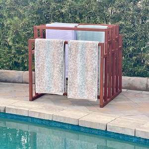 Könnte beinhalten: Ein Holz-Handtuchständer mit vier Handtüchern, die daran hängen. Die Handtücher sind weiß, hellblau und in einem hellblauen und braunen Muster. Der Ständer steht neben einem Schwimmbad.