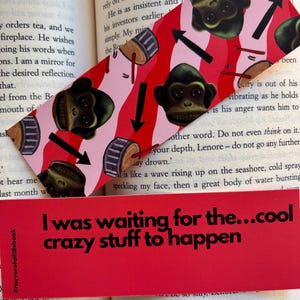 Può includere: Un segnalibro con un motivo rosso e bianco di facce di scimmia, tamburi e frecce. Sotto, un segnalibro rosso con il testo "I was waiting for the...cool crazy stuff to happen".