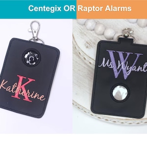 May include: Two black keychains with silver hardware. One keychain has the name "Katherine" embroidered in pink with a large pink "K". The other keychain has "Ms. Wyant" embroidered in purple with a large purple "W". The text "Centegix OR Raptor Alarms" is at the top.