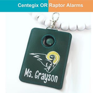 May include: A dark green key fob with a silver clasp and white beaded wristlet. The fob features an embroidered ram logo in white and yellow, with the name "Ms. Grayson" in white. The text "Centegix OR Raptor Alarms" is at the top.