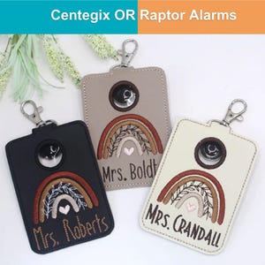May include: Three rectangular keychains in black, tan, and cream, each with a silver clasp. They feature a rainbow design with a heart and the name "Mrs. Roberts", "Mrs. Boldt", and "Mrs. Crandall". The text "Centegix OR Raptor Alarms" is at the top.