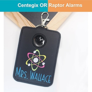 May include: Black leather key fob with a silver clasp. The fob features an embroidered atom design in pink, yellow, and green, with the name "MRS. WALLACE" in blue. The text "Centegix OR Raptor Alarms" is at the top.