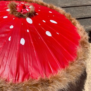 Pode incluir: Um guarda-sol vermelho com bolinhas brancas, assemelhando-se a um cogumelo. A borda &eacute; adornada com pele marrom. O guarda-sol est&aacute; aberto, mostrando a parte inferior.
