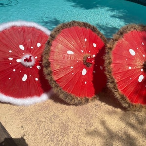 Pode incluir: Tr&ecirc;s guarda-s&oacute;is vermelhos com bolinhas brancas e acabamentos decorativos. Um guarda-sol tem acabamento em pele sint&eacute;tica branca, enquanto os outros dois t&ecirc;m acabamento em pele sint&eacute;tica castanha. Os guarda-s&oacute;is est&atilde;o dispostos sobre uma superf&iacute;cie de pedra.