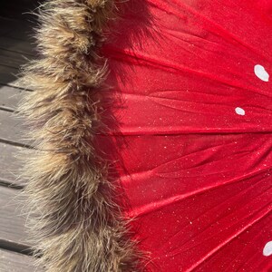 Pode incluir: Um close-up de um guarda-sol vermelho com acabamento em pele castanha e bolinhas brancas. O tecido do guarda-sol tem um acabamento brilhante e a borda de pele adiciona um toque de eleg&acirc;ncia. O design &eacute; atraente e &uacute;nico.