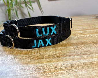 May include: Two black dog collars with silver hardware. The collars have the names "LUX" and "JAX" embroidered in turquoise thread. The collars are made of a durable, woven material.