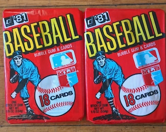 Può includere: Due pacchetti di carte da baseball rossi e bianchi con il testo "Baseball" in lettere gialle. Ogni pacchetto contiene 18 carte e una gomma da masticare. I pacchetti sono del 1981.