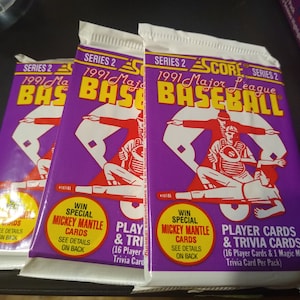 May include: Three packs of 1991 Score Major League Baseball cards. The packs are purple and feature a cartoon image of baseball players. The packs are labeled "Series 2" and "1991 Major League Baseball".