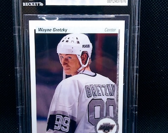 Puede incluir: Una tarjeta de hockey de Wayne Gretzky del set Upper Deck de 1990-91. La tarjeta está calificada con un 9 por Beckett Grading Services y presenta una foto de Gretzky con su uniforme de los Kings de Los Ángeles. La tarjeta está en una caja de plástico protectora.
