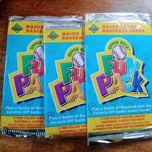 May include: Three unopened packs of Upper Deck Fun Pack Major League Baseball cards. The packs are blue and yellow with the words "Fun Pack" in large, colorful letters. The packs feature a baseball card game with scratch-off game insert cards.