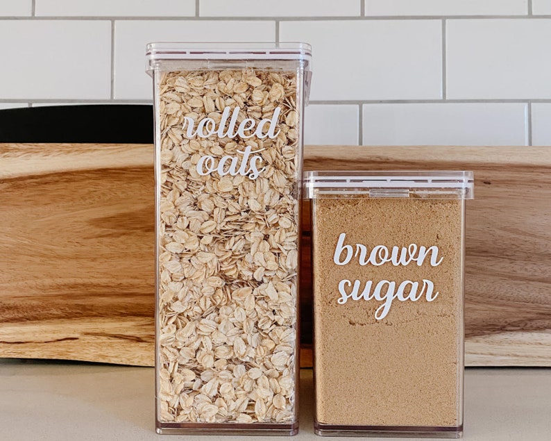 May include: Two clear plastic containers with lids, one filled with rolled oats and labeled "rolled oats", the other filled with brown sugar and labeled "brown sugar".