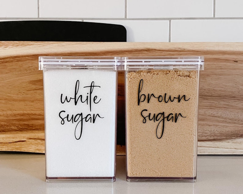 May include: Two clear plastic containers with labels that say "white sugar" and "brown sugar".