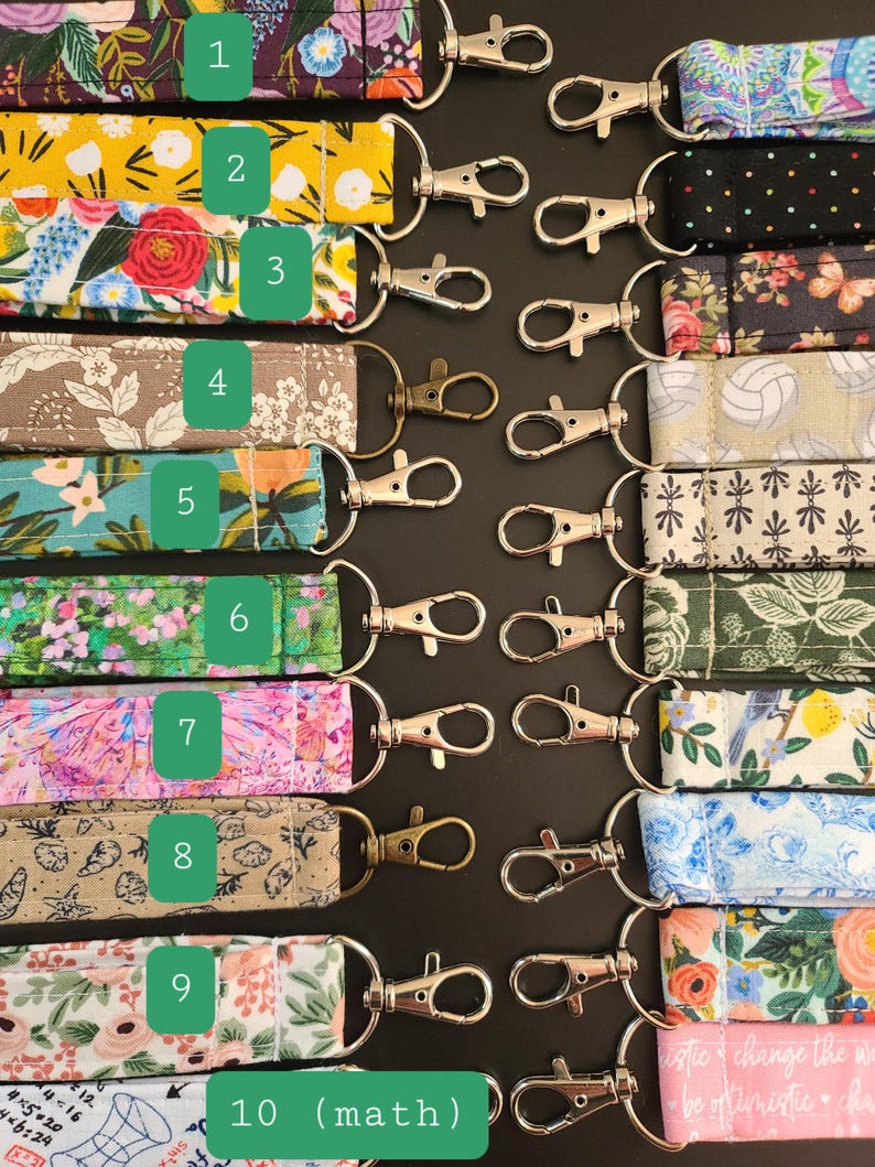 May include: A collection of fabric keychains with various patterns, including floral, geometric, and abstract designs. Each keychain features a metal clasp for easy attachment. The keychains are arranged on a dark surface.