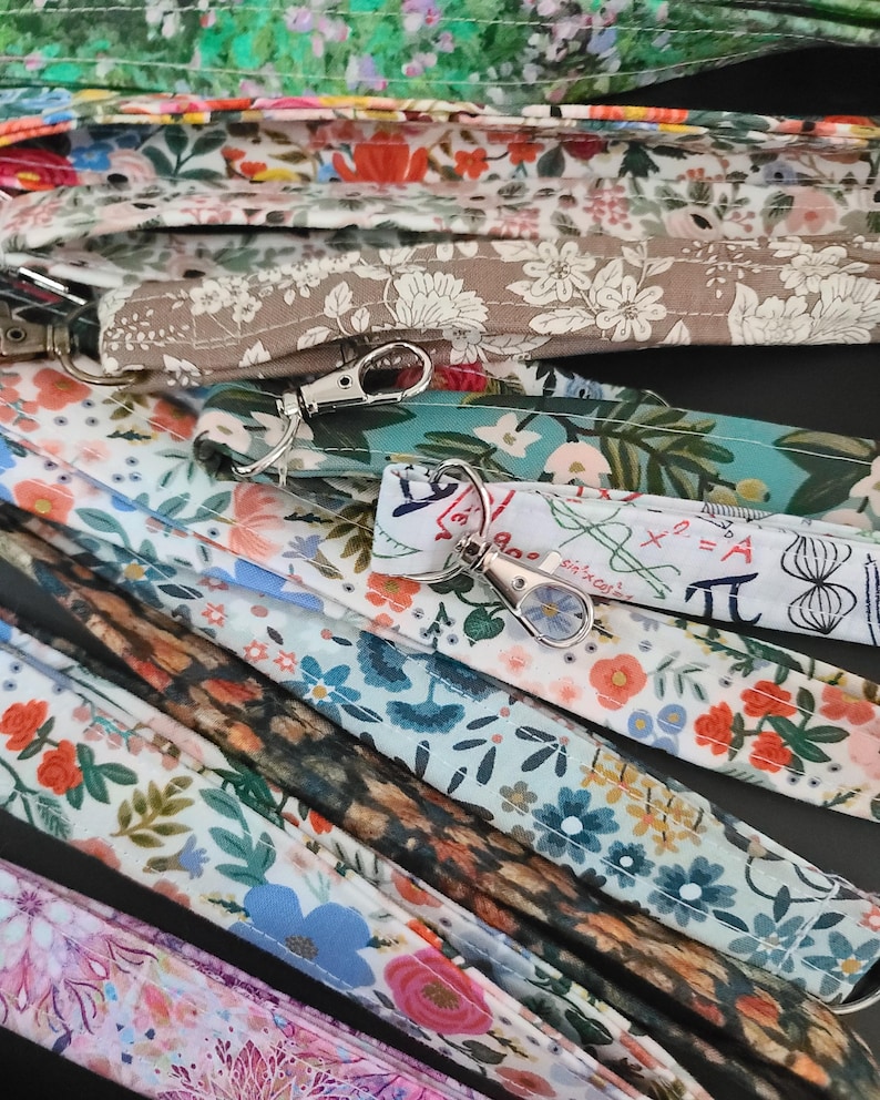 May include: A collection of patterned lanyards with metal swivel clasps. The lanyards feature various floral and botanical designs in shades of pink, blue, green, and brown. Some lanyards have a white background with mathematical symbols.