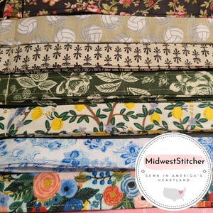 May include: A collection of fabric lanyards with various patterns, including floral, volleyballs, and polka dots. The lanyards are in a variety of colors, including black, pink, green, and blue. The text "change the world be you be fearless" is visible on a pink lanyard.