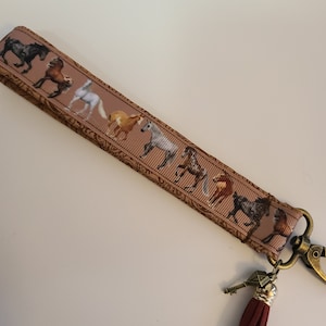 May include: A brown key chain with a horse print design and a burgundy tassel. The key chain has a metal clasp and a key charm.