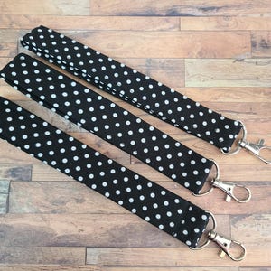 May include: Three black and white polka dot lanyards with silver-colored swivel hooks. The lanyards are made of fabric and are displayed on a wooden surface. The polka dots are white and evenly spaced.