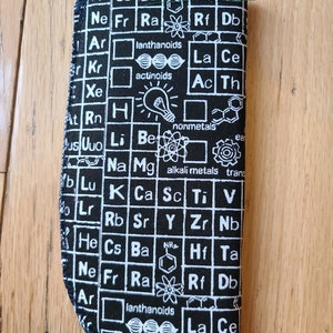May include: Black fabric pouch with a white periodic table print. The pouch features the chemical symbols and names of elements, including lanthanoids and actinoids.