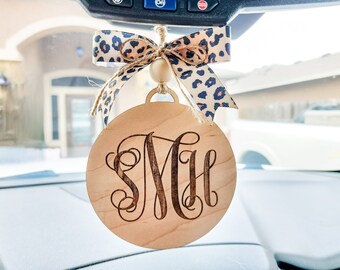 May include: A wooden car air freshener with a leopard print bow and the monogram "SMH" engraved on the front.