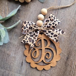 May include: Wooden monogram ornament with a leopard print bow and wooden beads. The monogram is the letter "B".