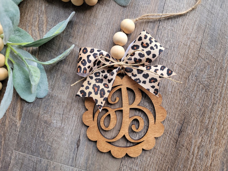May include: Wooden monogram ornament with a leopard print bow and wooden beads. The monogram is the letter "B".