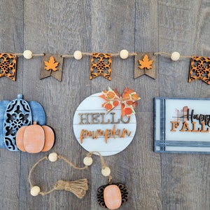 May include: A fall-themed craft decor set with a wooden sign that says "Hello Pumpkin", a wooden sign that says "Happy Fall", and a string of wooden flags with fall-themed designs.