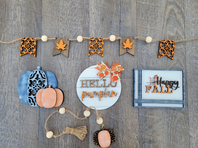 May include: A fall-themed craft decor set with a wooden sign that says "Hello Pumpkin", a wooden sign that says "Happy Fall", and a string of wooden flags with fall-themed designs.
