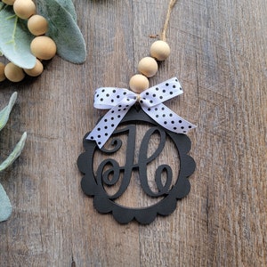 May include: Black wooden monogram ornament with a white and black polka dot bow. The letter "H" is cut out of the center of the ornament.