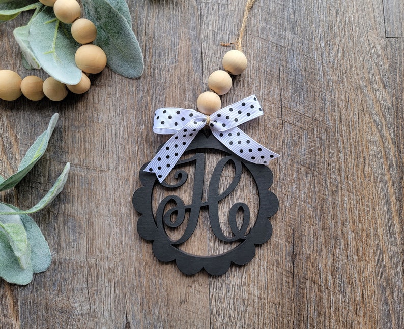 May include: Black wooden monogram ornament with a white and black polka dot bow. The letter "H" is cut out of the center of the ornament.
