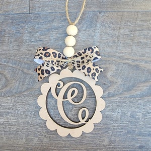 May include: Wooden door hanger with a scalloped edge and the letter "C" cut out. The hanger is decorated with a leopard print ribbon bow and wooden beads.