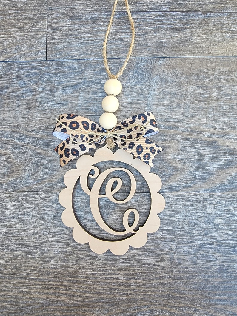 May include: Wooden door hanger with a scalloped edge and the letter "C" cut out. The hanger is decorated with a leopard print ribbon bow and wooden beads.