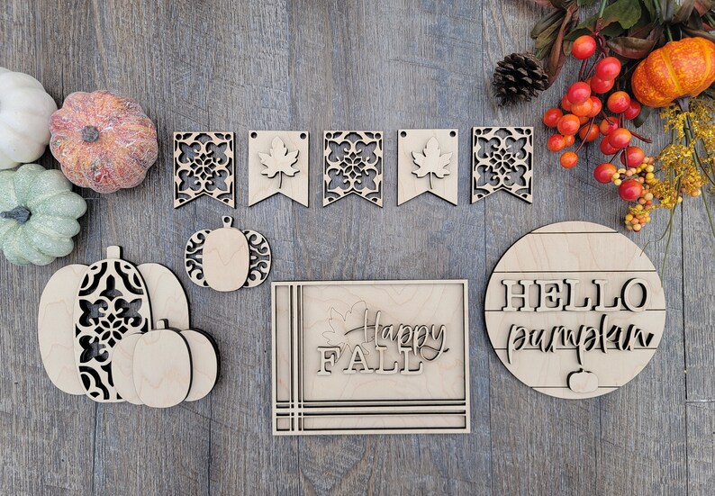 May include: A set of wooden fall-themed decorations, including a "Happy Fall" sign, a "Hello Pumpkin" sign, and a pumpkin banner with leaf and floral cutouts.
