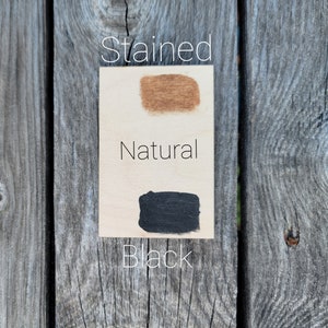May include: A close-up of three wood samples showing different finishes: stained, natural, and black. The samples are arranged vertically on a wooden surface.