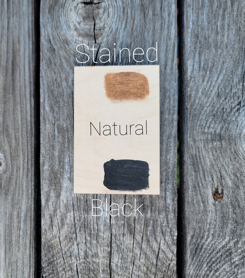 May include: A close-up of three wood samples showing different finishes: stained, natural, and black. The samples are arranged vertically on a wooden surface.