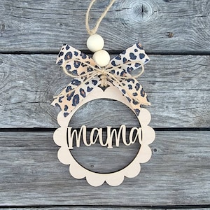 May include: A wooden sign with the word "mama" written in cursive. The sign is decorated with a brown and black leopard print ribbon and wooden beads.