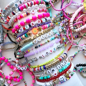 May include: A collection of colourful beaded bracelets with various words and phrases, including "Fearless", "Friend", "Love", and "Smile".