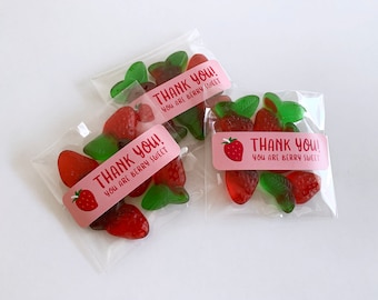Op de afbeelding: Drie doorzichtige plastic zakjes gevuld met rode en groene gummy snoepjes in de vorm van aardbeien en bladeren. Elk zakje heeft een roze sticker met de tekst "THANK YOU! YOU ARE BERRY SWEET" in rood en wit.