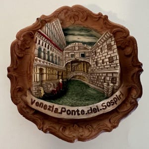 May include: A circular terracotta-colored wall plaque featuring a three-dimensional relief of the Bridge of Sighs in Venice. The scene includes a canal, a gondola, and stone buildings. A banner at the bottom displays the text Venezia.Ponte.dei.Sospiri.