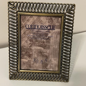Op de afbeelding: Een rechthoekige fotolijst met een metalen messing afwerking en een gedraaide, touwachtige rand. De inleg toont de tekst "connoisseur", "DECORATIVE PHOTO FRAME" en "9cm x 13cm". De lijst heeft een klassiek, gestructureerd ontwerp.