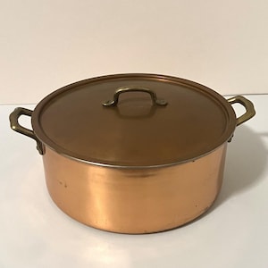 以下が含まれることがあります： 真鍮製のサイドハンドル2つと蓋が付いた円形の銅鍋。鍋は磨かれた金属仕上げで、蓋の中央には真鍮製のハンドルが付いています。デザインはシンプルで機能的であり、調理器具の外面全体に銅素材の温かみのある赤褐色の色調が際立っています。