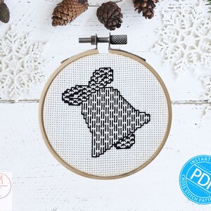May include: A black and white cross stitch pattern of a stylized reindeer in a hoop. The hoop is on a white wooden surface with pine branches and snowflakes.