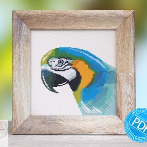 May include: Cross stitch pattern of a blue and yellow macaw with a white background. The pattern is in a wooden frame and there is a blue circle with the word "PDF" in white text and the words "Instant Download Counted Cross Stitch Pattern" around the circle.