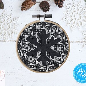 May include: A black and white cross stitch pattern of a snowflake in a wooden embroidery hoop. The pattern is surrounded by white snowflakes on a white wooden background. The text "INSTANT DOWNLOAD PDF CROSS STITCH PATTERN" is on a blue circle.