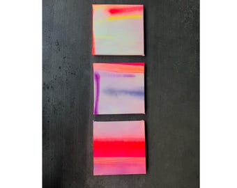 May include: Three abstract paintings with a watercolor style. The top painting is a light blue with yellow and red accents. The middle painting is a light purple with blue and red accents. The bottom painting is a light pink with red and purple accents.