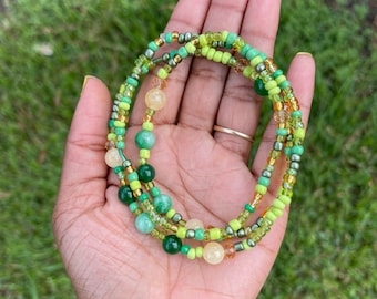 May include: A multi-strand beaded necklace with green, yellow, and brown beads. The necklace is made of different sizes and shapes of beads, including round, oval, and square beads.