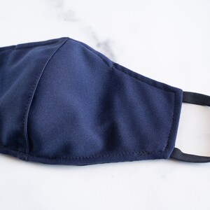 May include: A dark blue face mask with black elastic ear loops. The mask is made of a soft, breathable fabric.